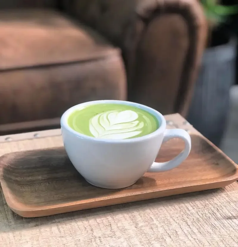 Matcha latte con dibujo en taza blanca sobre bandeja de madera