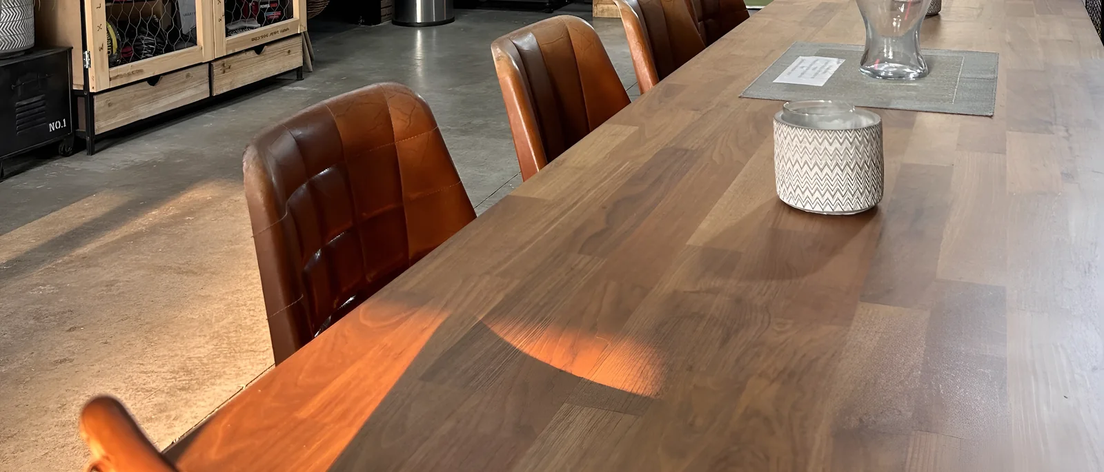 La mesa larga de madera de La Calma con sillas de cuero y el sol de la tarde sobre el suelo de hormigón