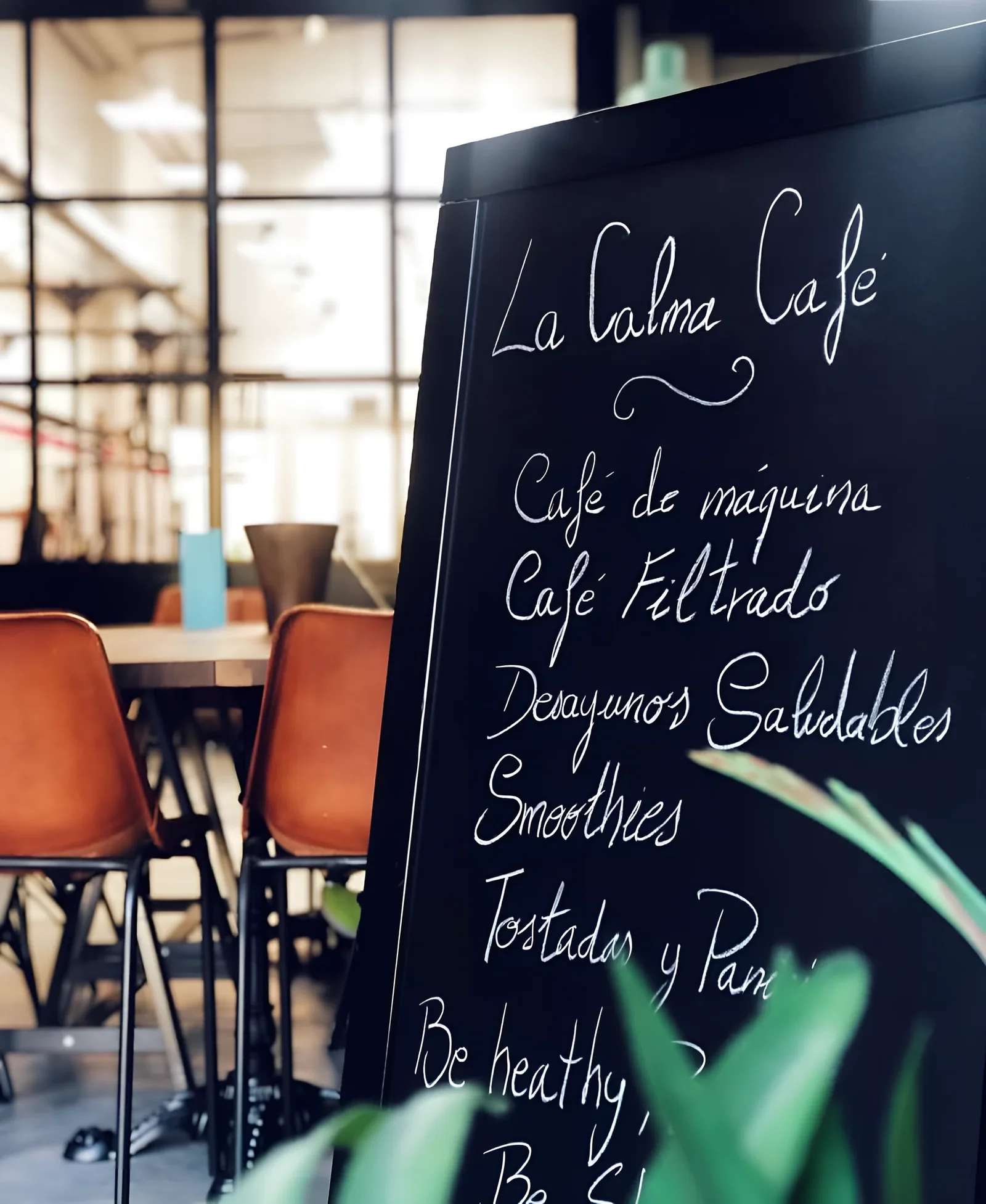 La pizarra de La Calma Café con la carta escrita a tiza, junto a las sillas de cuero y el ventanal