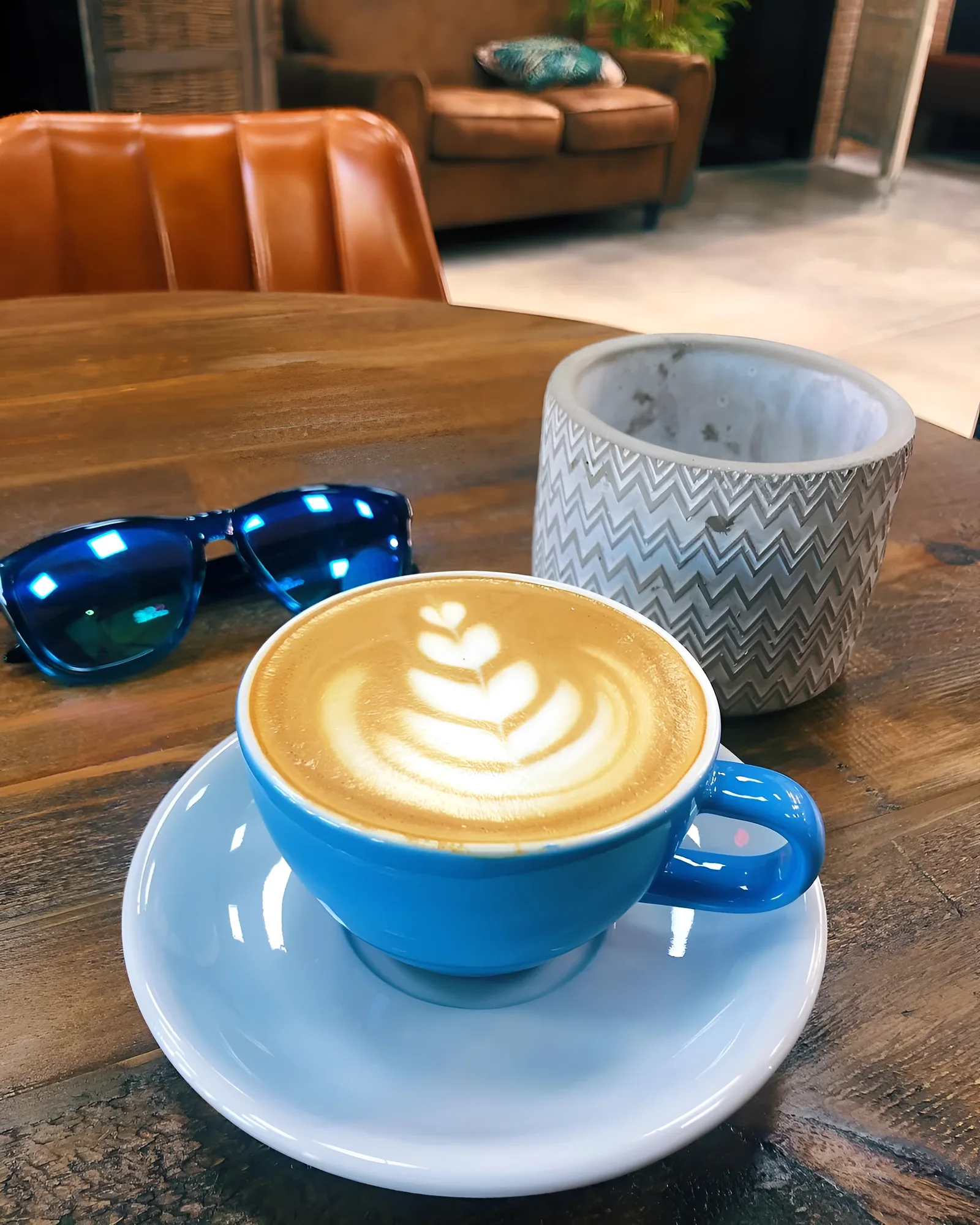 Café con leche en taza azul sobre una mesa de madera, junto a una silla de cuero